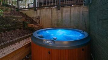 A hot tub with a control panel, surrounded by a wooden deck and a concrete wall.