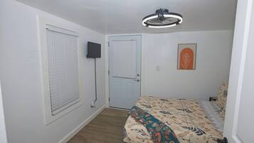 A bedroom with a bed, a door, a wall-mounted TV, and a ceiling light fixture.