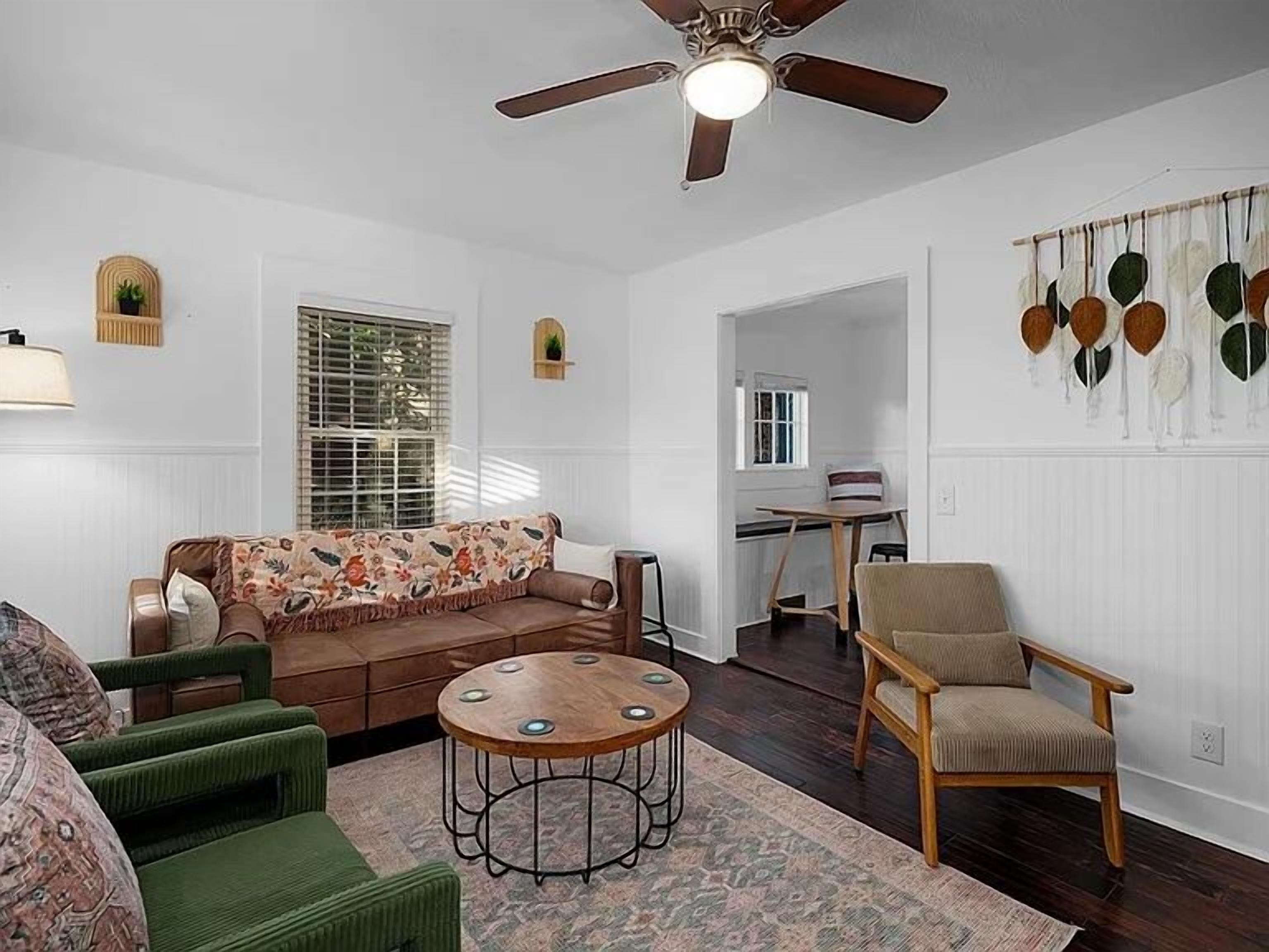 A living room with a brown sofa, a green armchair, a wooden coffee table, and a ceiling fan.