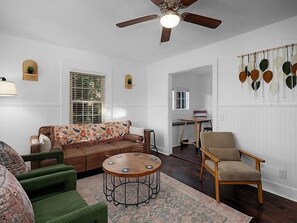 A living room with a brown sofa, a green armchair, a wooden coffee table, and a ceiling fan. - Messer Manor - Downtown, Walk to Shops (Blue Ridge)