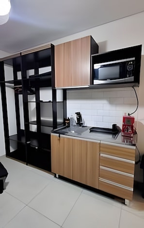 A compact kitchen with a microwave, a sink, and wooden cabinets. - Salles Residence Barra Funda (São Paulo)
