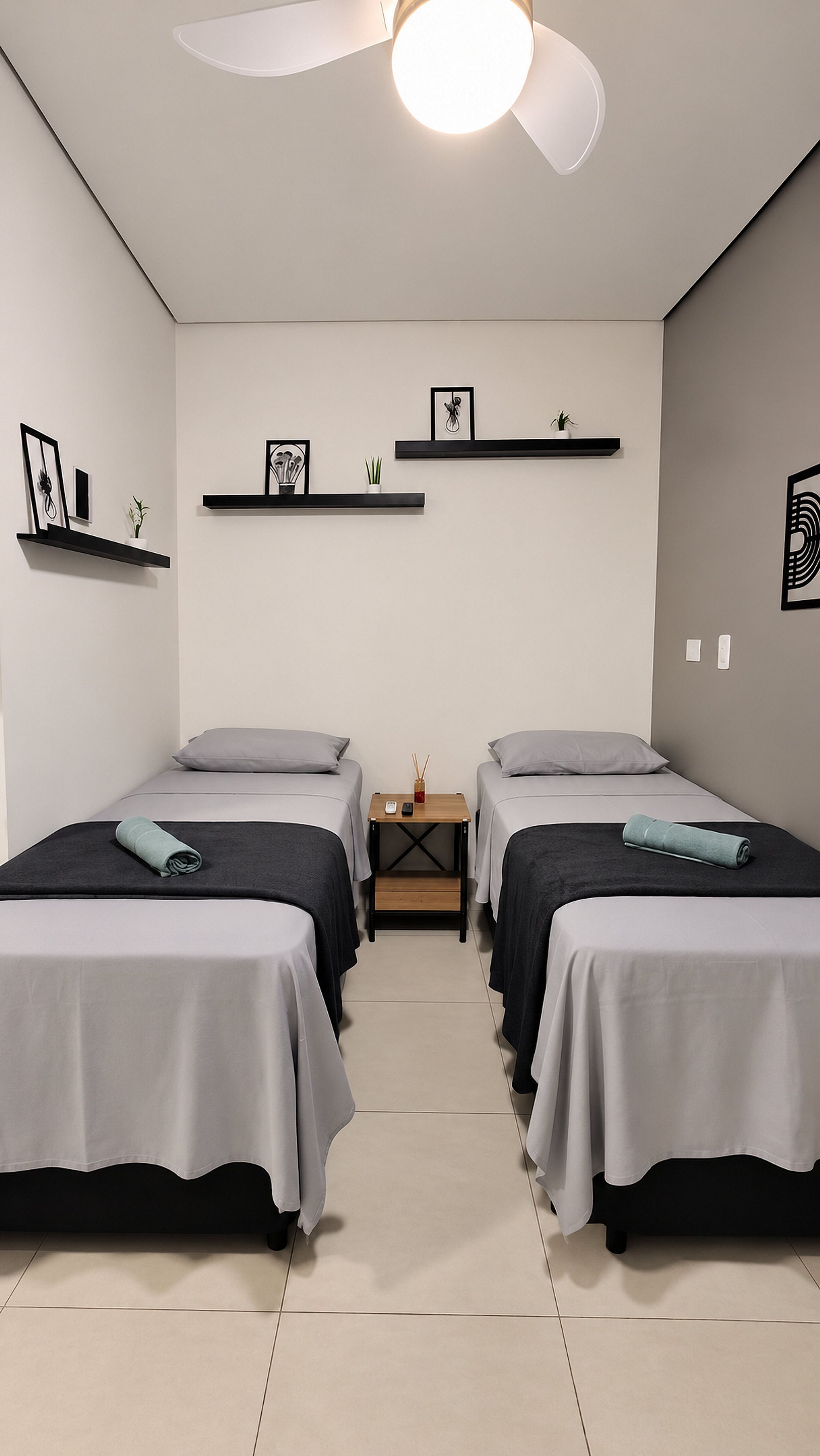 A hotel room with two beds, a ceiling fan, a small table with a phone and a candle, and wall-mounted shelves with pictures and plants.