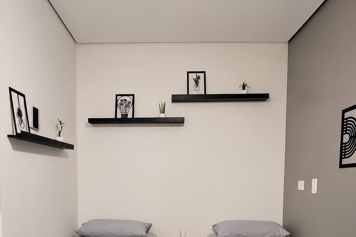 A hotel room with two beds, a ceiling fan, a small table with a phone and a candle, and wall-mounted shelves with pictures and plants.