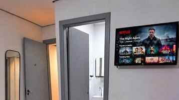 Uma sala de estar moderna com uma TV de tela plana na parede exibindo a interface da Netflix.