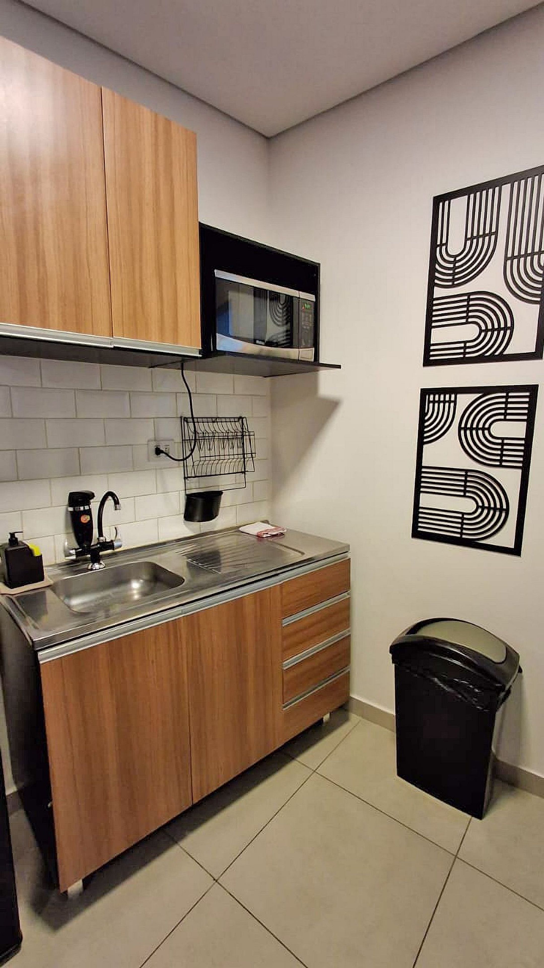 A compact kitchen with wooden cabinets, a microwave, a sink, and a trash bin.