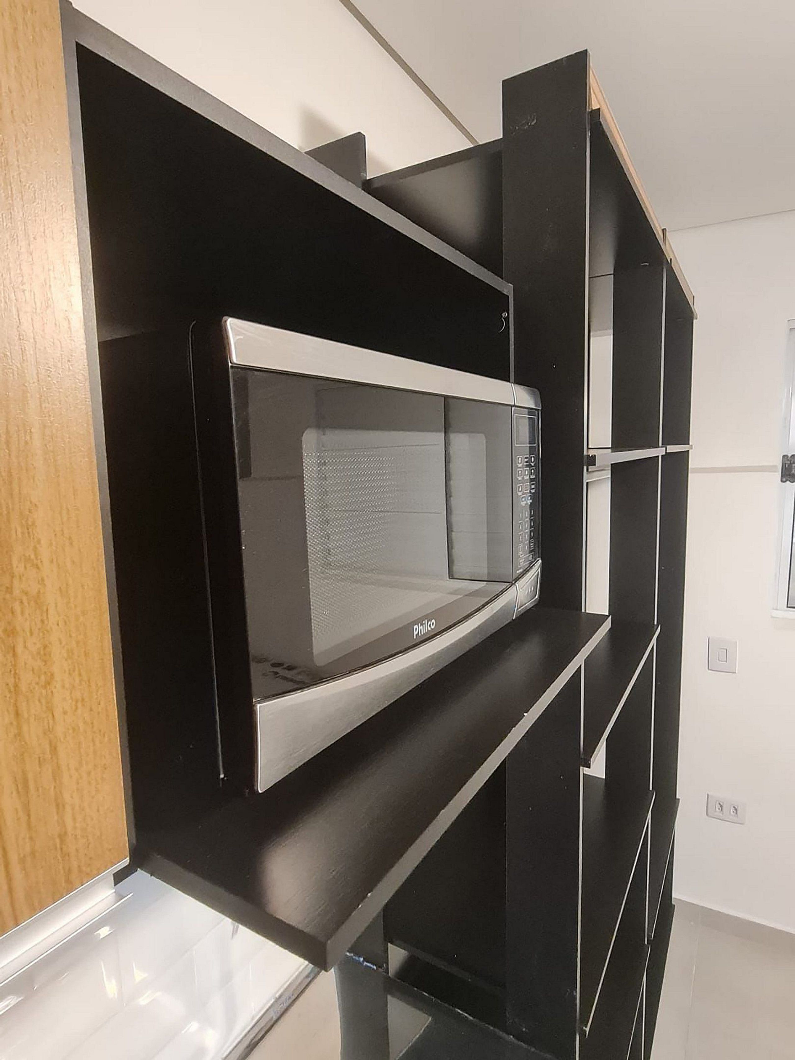 A modern kitchen with a built-in microwave, black cabinetry, and a wooden countertop.