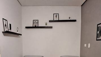 A room with two beds, a bedside table, a nightstand, and wall-mounted shelves with framed pictures.