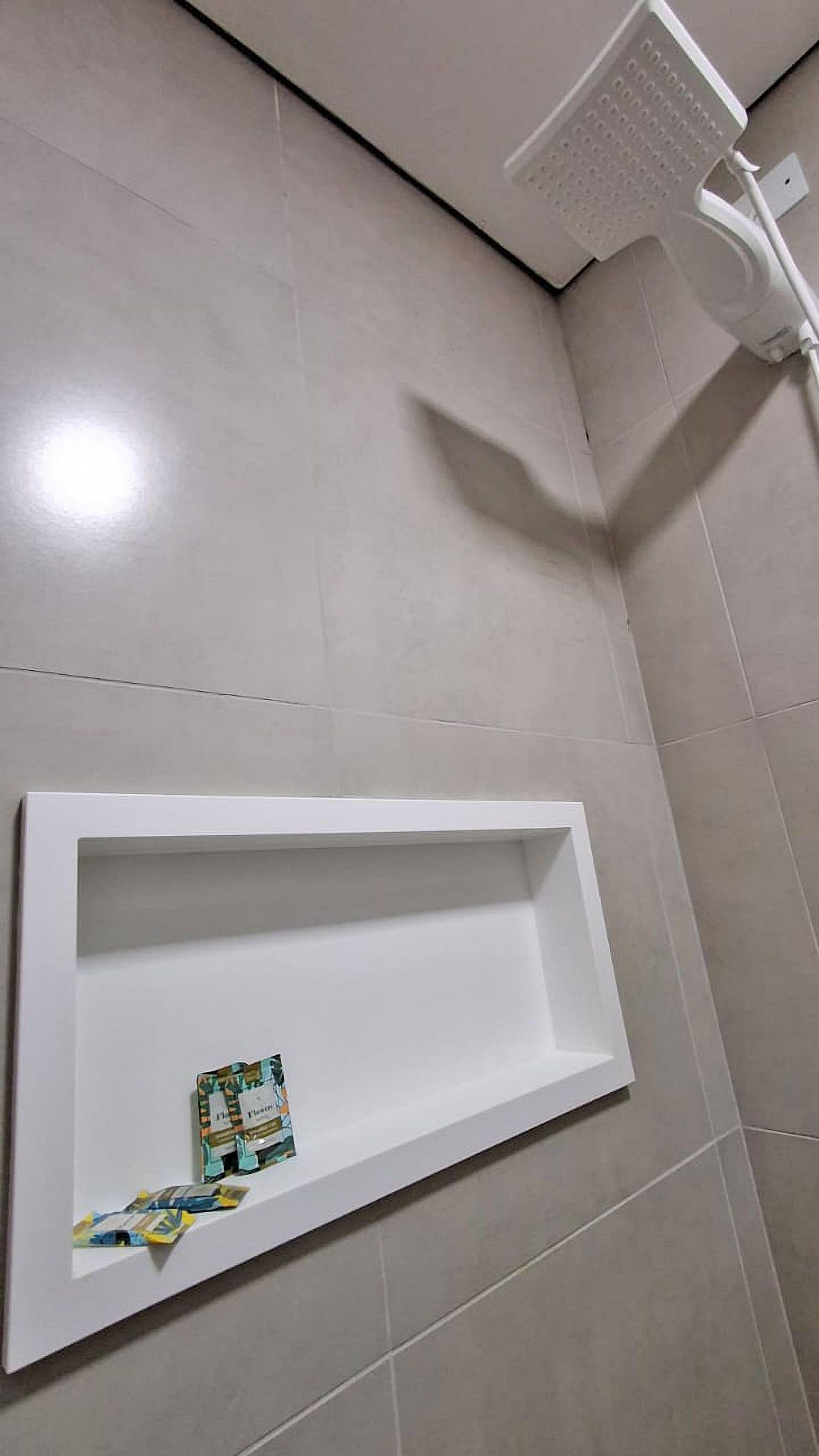 A bathroom with a shower, a white shelf, and tiled walls.