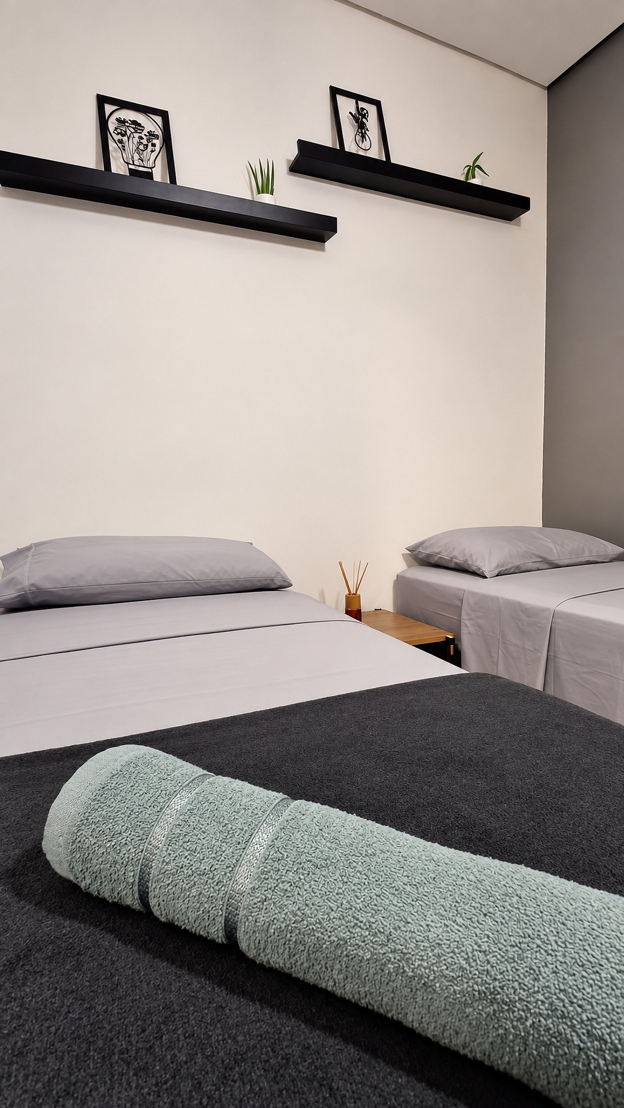 A modern bedroom with two beds, a small table, and wall-mounted shelves with decorative items.