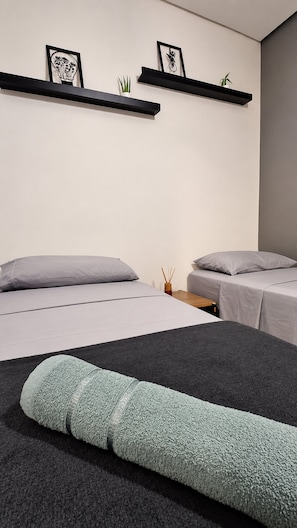 A modern bedroom with two beds, a small table, and wall-mounted shelves with decorative items.