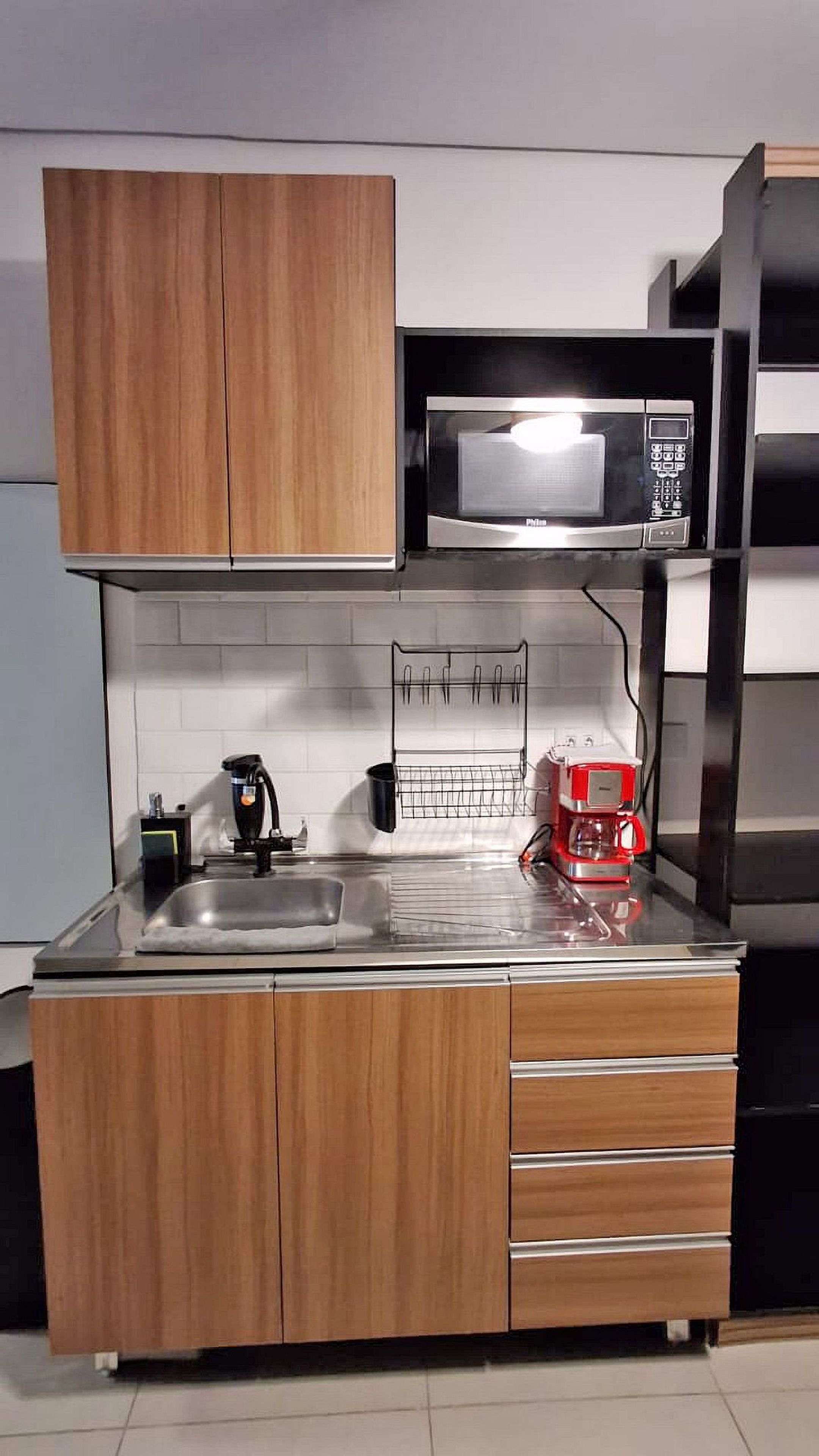 A compact kitchen with wooden cabinets, a microwave, a coffee machine, and a sink.