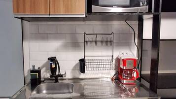 A compact kitchen with wooden cabinets, a microwave, a coffee machine, and a sink.