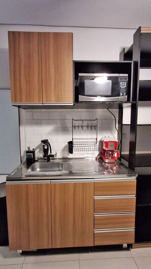 A compact kitchen with wooden cabinets, a microwave, a coffee machine, and a sink. - Salles Residence Barra Funda (São Paulo)