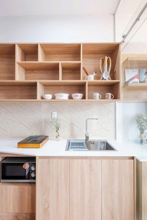 A modern kitchen with wooden cabinetry, a built-in microwave, and a stainless steel sink. - TMH HOUSE 03 LVT Hotel & Apartment (Son Tra)