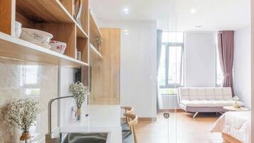 A modern kitchen with a built-in sink, wooden shelves, and a dining area with a white sofa and a small table.