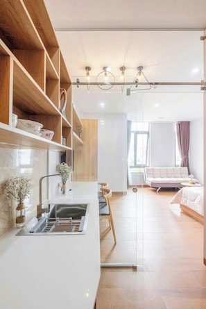 A modern kitchen with a built-in sink, wooden shelves, and a dining area with a white sofa and a small table. - TMH HOUSE 03 LVT Hotel & Apartment (Son Tra)