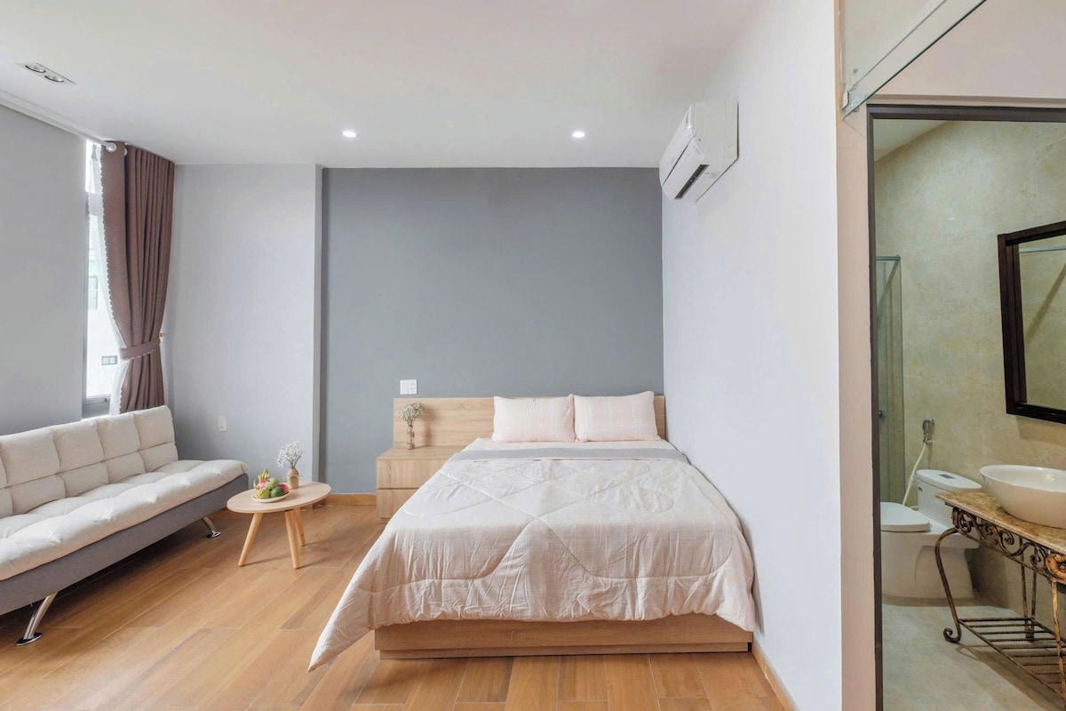 A bedroom with a bed, a sofa, a small table, and a bathroom with a sink and mirror.