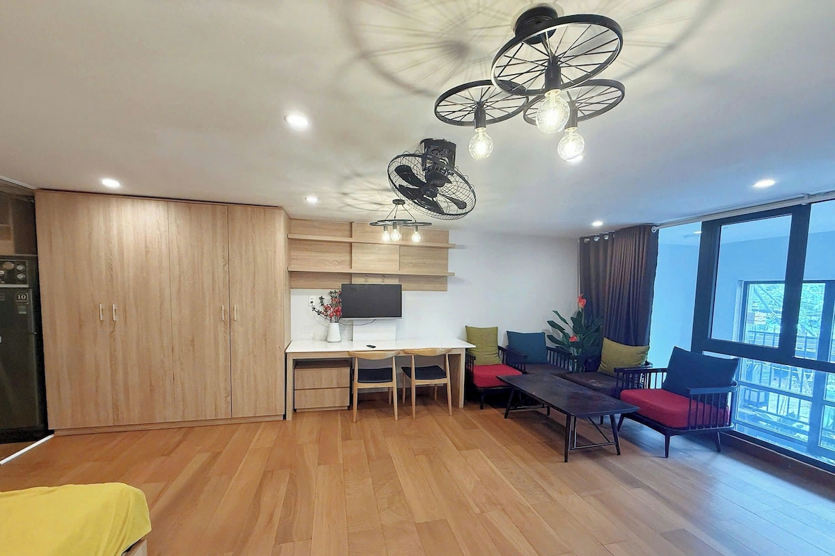 A modern kitchen with a dining area, wooden cabinets, a TV, and a large window.