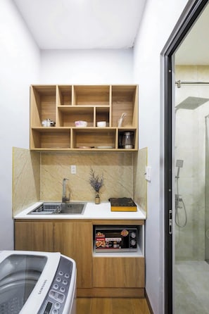 Cozinha compacta com micro-ondas embutido, cafeteira e prateleira com louças.