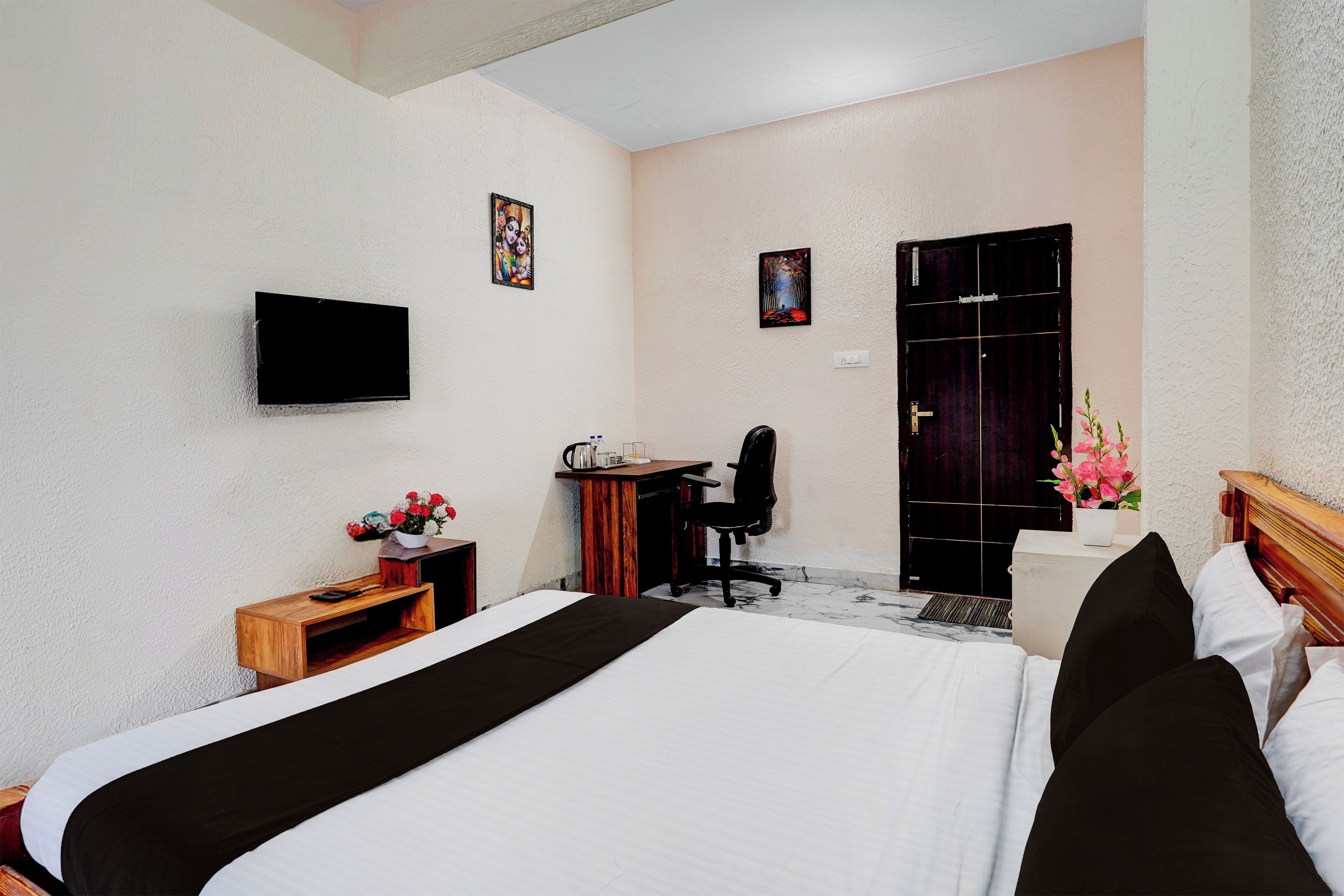Quarto de hotel com cama, escrivaninha, cadeira e televisão fixada na parede.