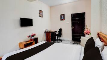 Quarto de hotel com cama, escrivaninha, cadeira e televisão fixada na parede.