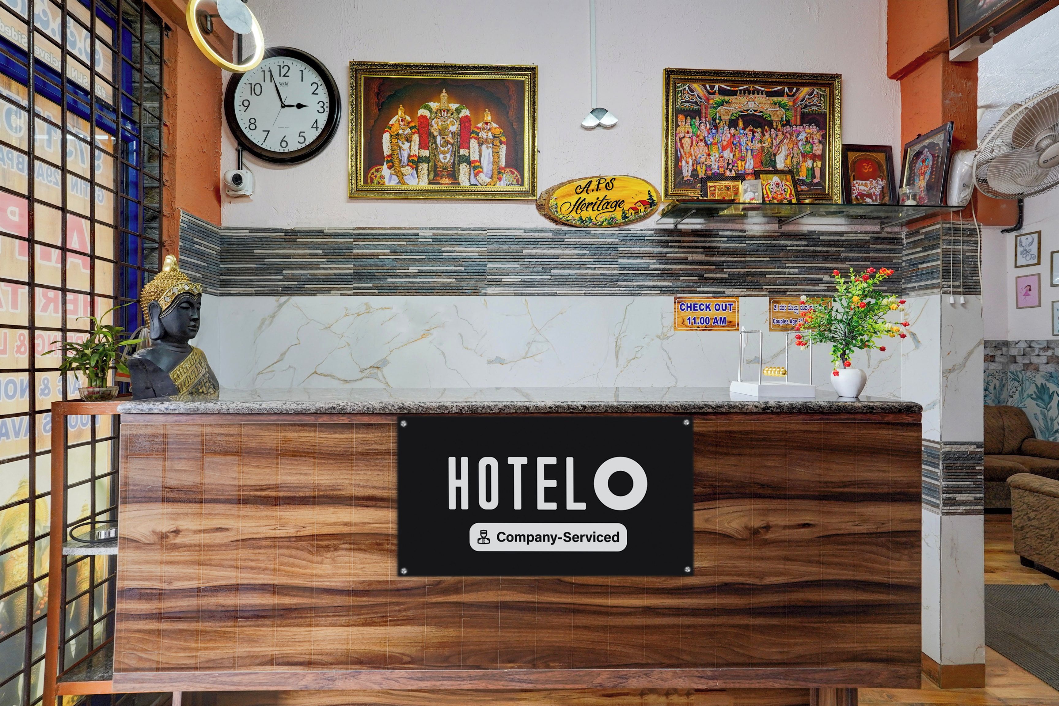 A hotel reception desk with a clock, framed religious paintings, and a sign indicating company-serviced rooms.