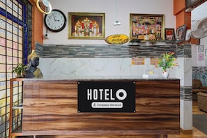 Mostrador de recepción de hotel con un reloj, cuadros religiosos enmarcados y un letrero que indica habitaciones de servicio de la empresa.