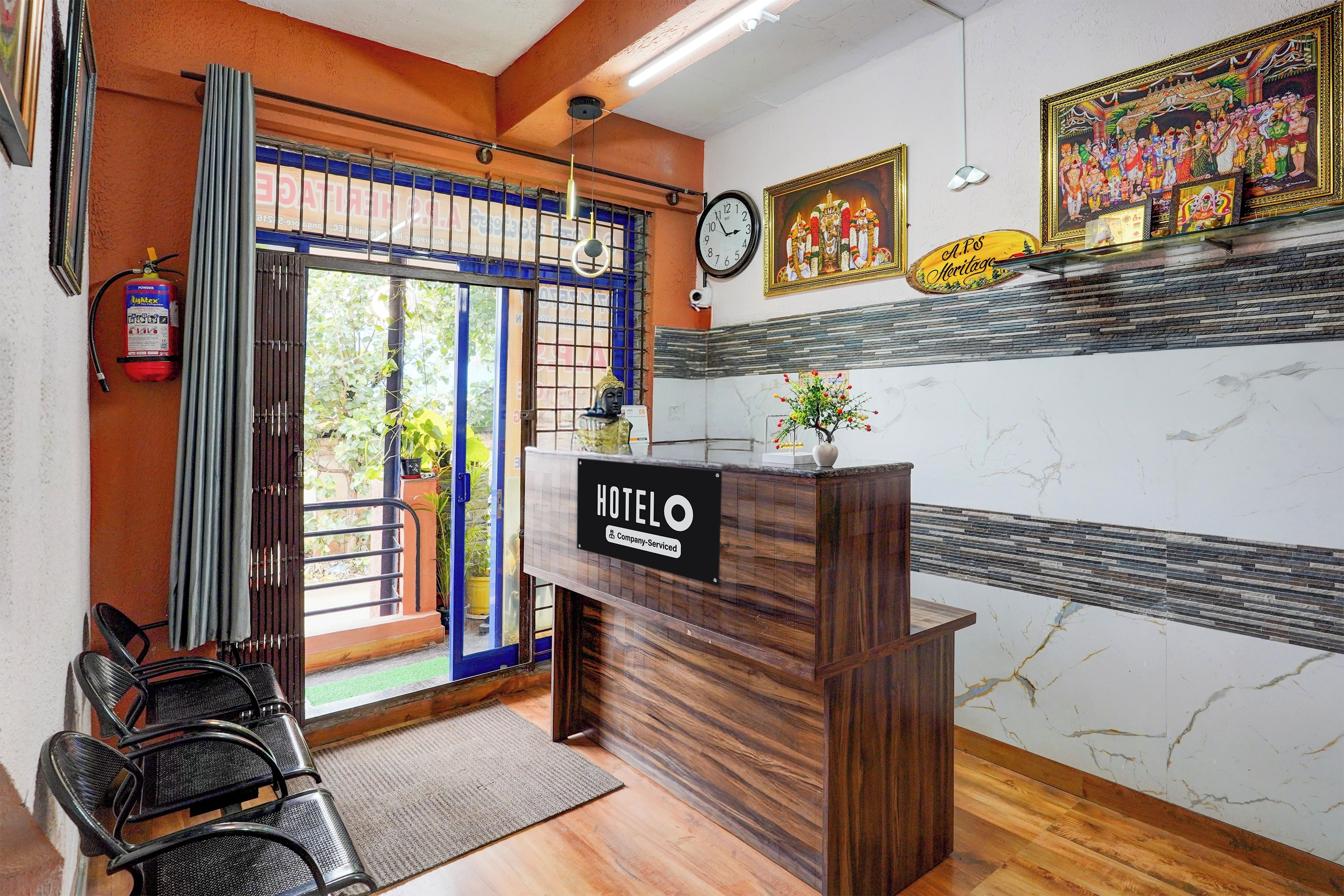 A hotel reception area with a wooden reception desk, a clock, and a sign indicating it is a company-serviced hotel.