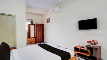 Habitación de hotel con cama, televisor montado en la pared, armario de madera y una mesita con un florero.