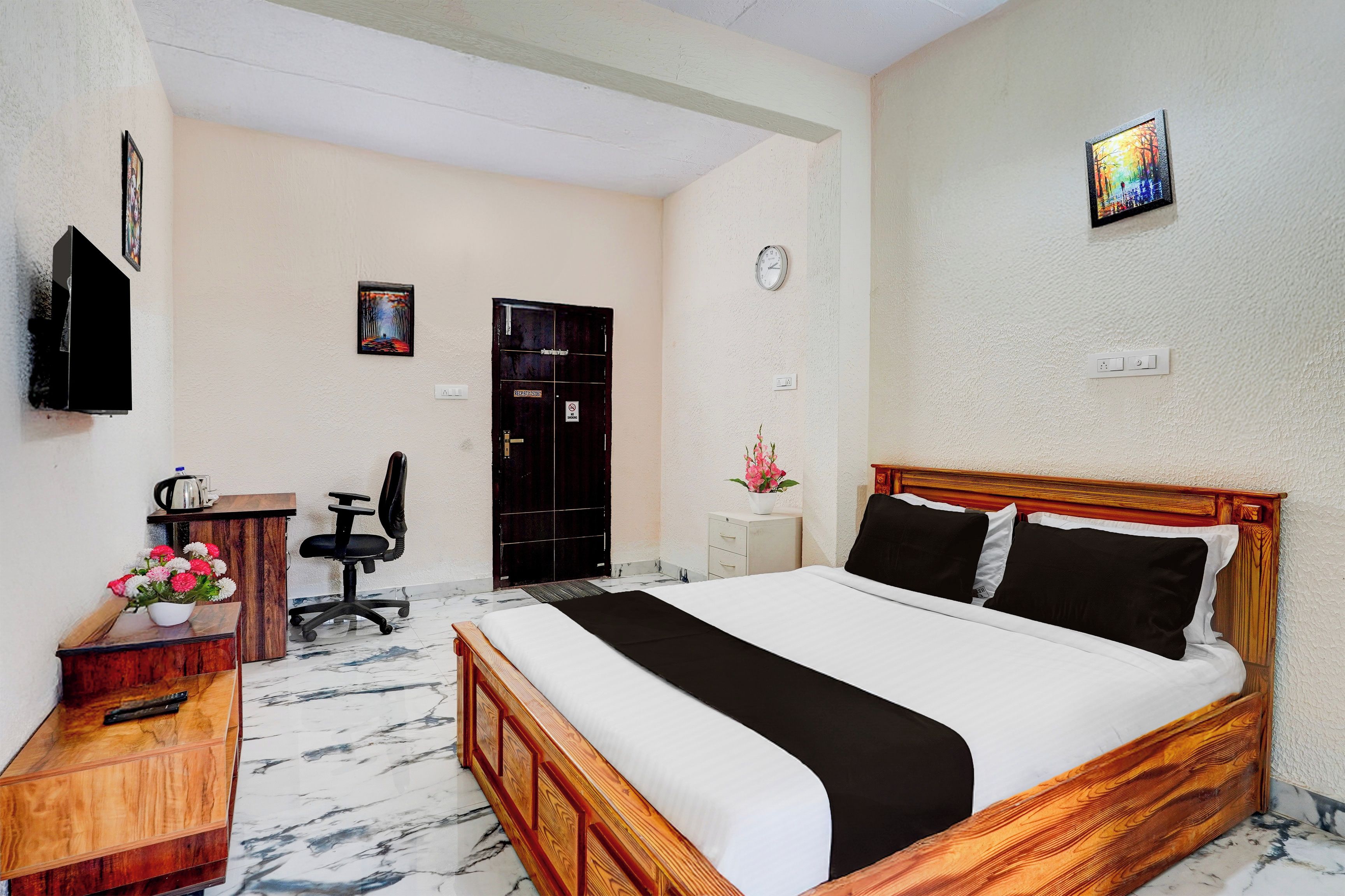 Une chambre d’hôtel avec un lit, un bureau, une chaise, une télévision, une horloge et une porte.