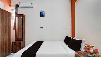 Una habitación de hotel con una cama, un armario de madera, un equipo de aire acondicionado, un interruptor de luz en la pared y un pequeño cuadro enmarcado.