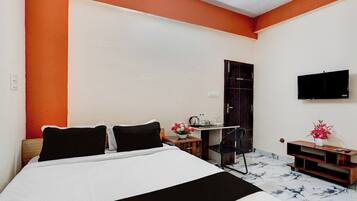 A hotel room with a bed, a desk, a chair, a TV, and a small table with flowers.