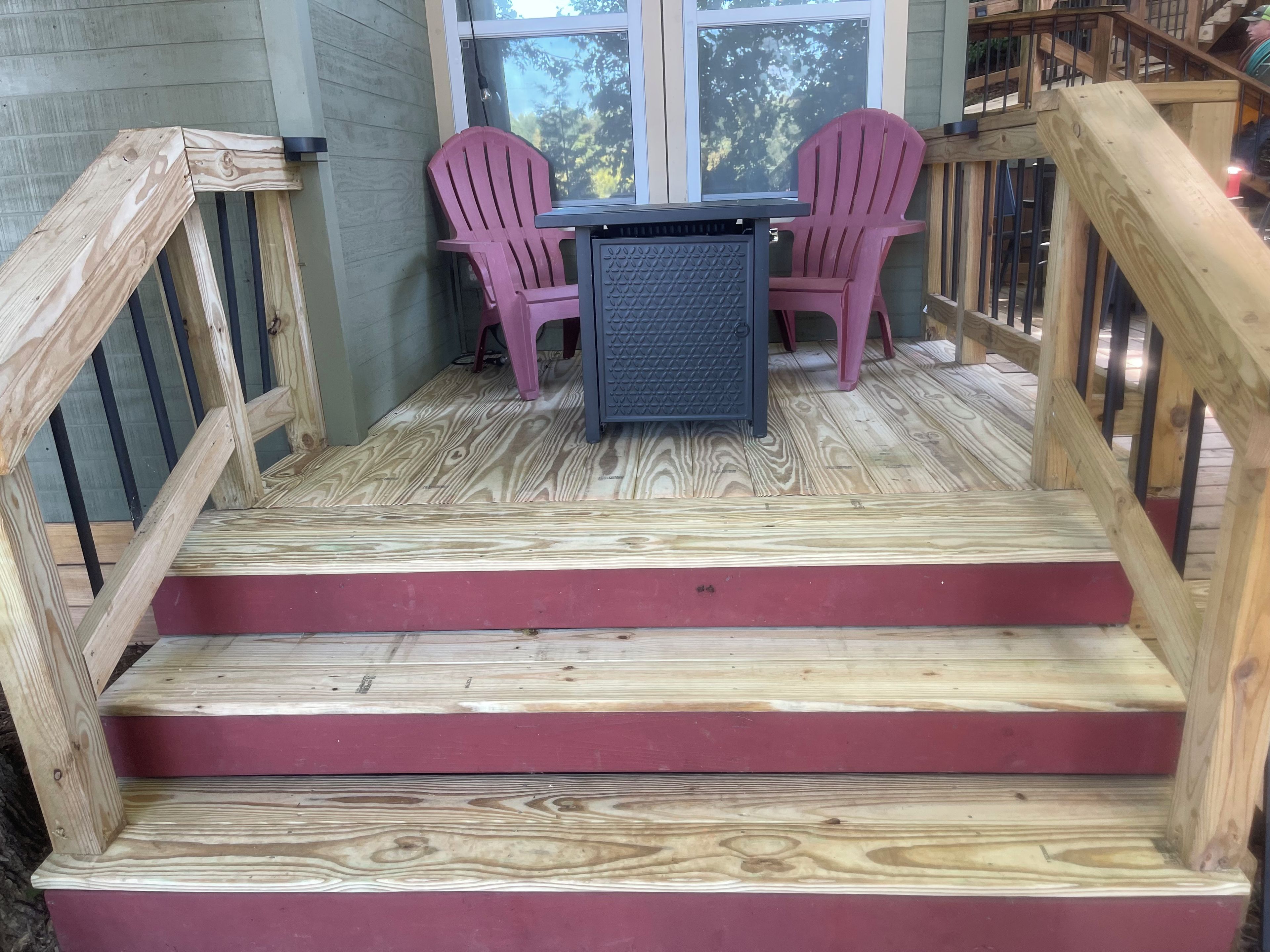 A wooden deck with a table and two chairs, a staircase with red steps, and a railing.