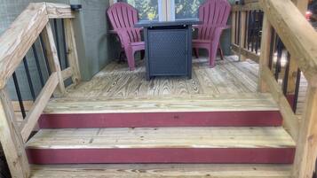 A wooden deck with a table and two chairs, a staircase with red steps, and a railing.