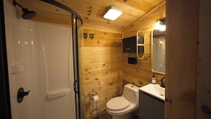 Een houten badkamer in een vakantiehuisje, met douche, toilet en wastafel.