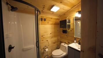 A wooden cabin bathroom with a shower, toilet, and sink.