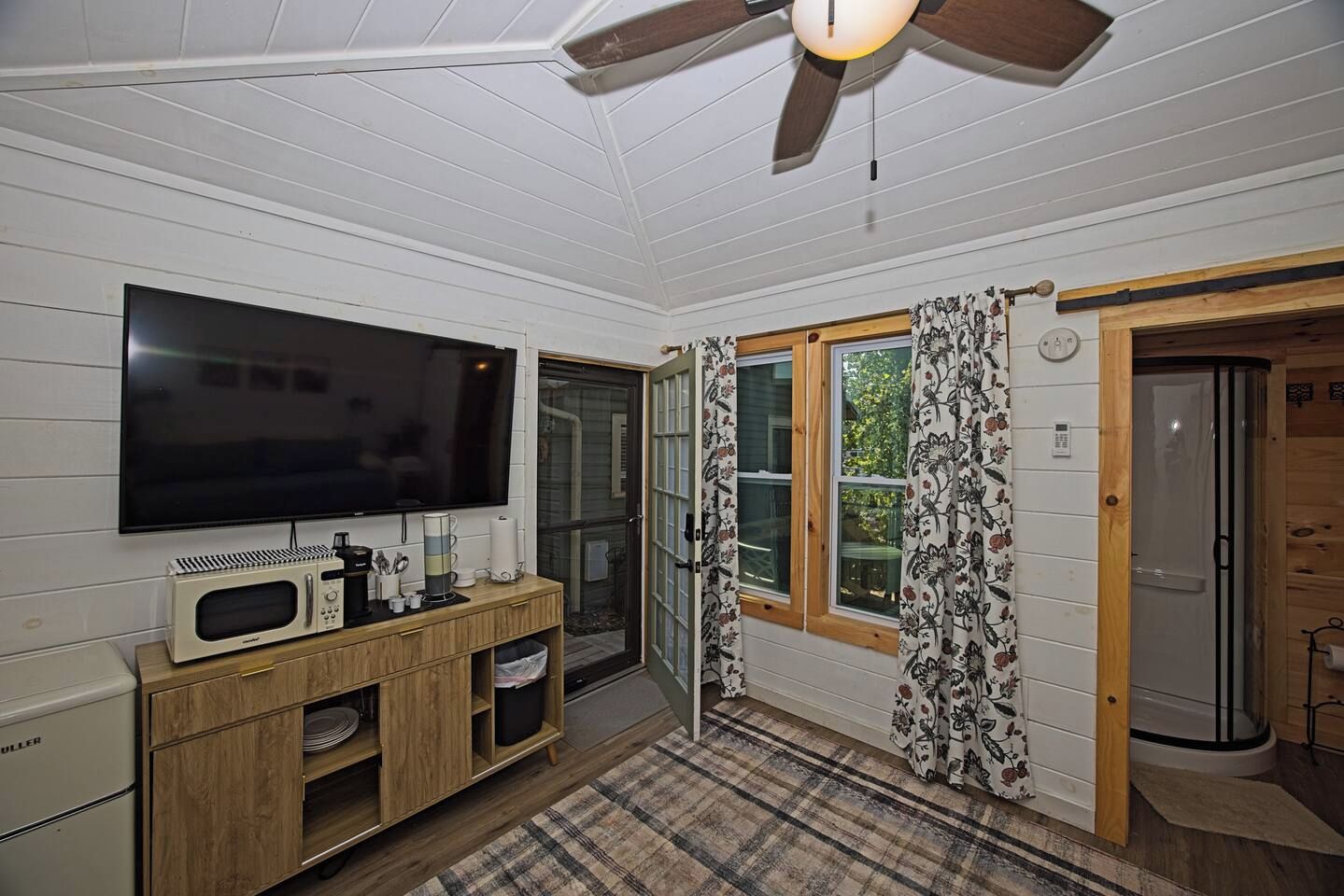 A room with a flat-screen TV, a wooden cabinet, a microwave, and a ceiling fan.