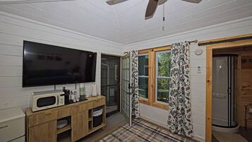 A room with a flat-screen TV, a wooden cabinet, a microwave, and a ceiling fan.