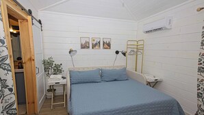 Een slaapkamer met een bed, nachtkastje, lamp, wanddecoratie en een airconditioning.