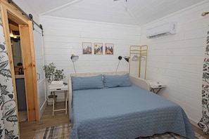 A bedroom with a bed, bedside table, lamp, wall art, and an air conditioning unit. - Mini Messer - Downtown, Walk to Shops (Blue Ridge)