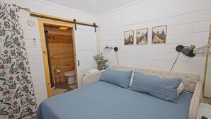 Een slaapkamer met een bed, een houten deur, een toilet en een wandlamp.