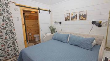 A bedroom with a bed, a wooden door, a toilet, and a wall-mounted lamp.