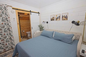 A bedroom with a bed, a wooden door, a toilet, and a wall-mounted lamp. - Mini Messer - Downtown, Walk to Shops (Blue Ridge)