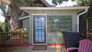 A covered outdoor area with a door, a bench, a trash bin, and a wall covered in foliage.
