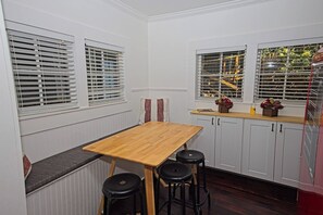 A compact kitchen with a wooden table and bar stools, white cabinetry, and a window with blinds. - Messer Loop Hideaway - Downtown, Walk to Shops (Blue Ridge)