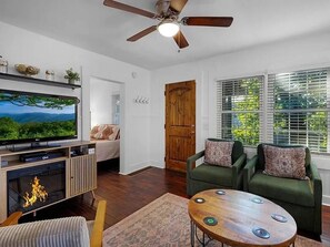 A living room with a television, fireplace, green sofa, and a ceiling fan. - Messer Loop Hideaway - Downtown, Walk to Shops (Blue Ridge)