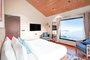 Een slaapkamer met een bed, een stoel, een televisie en een groot raam met uitzicht.