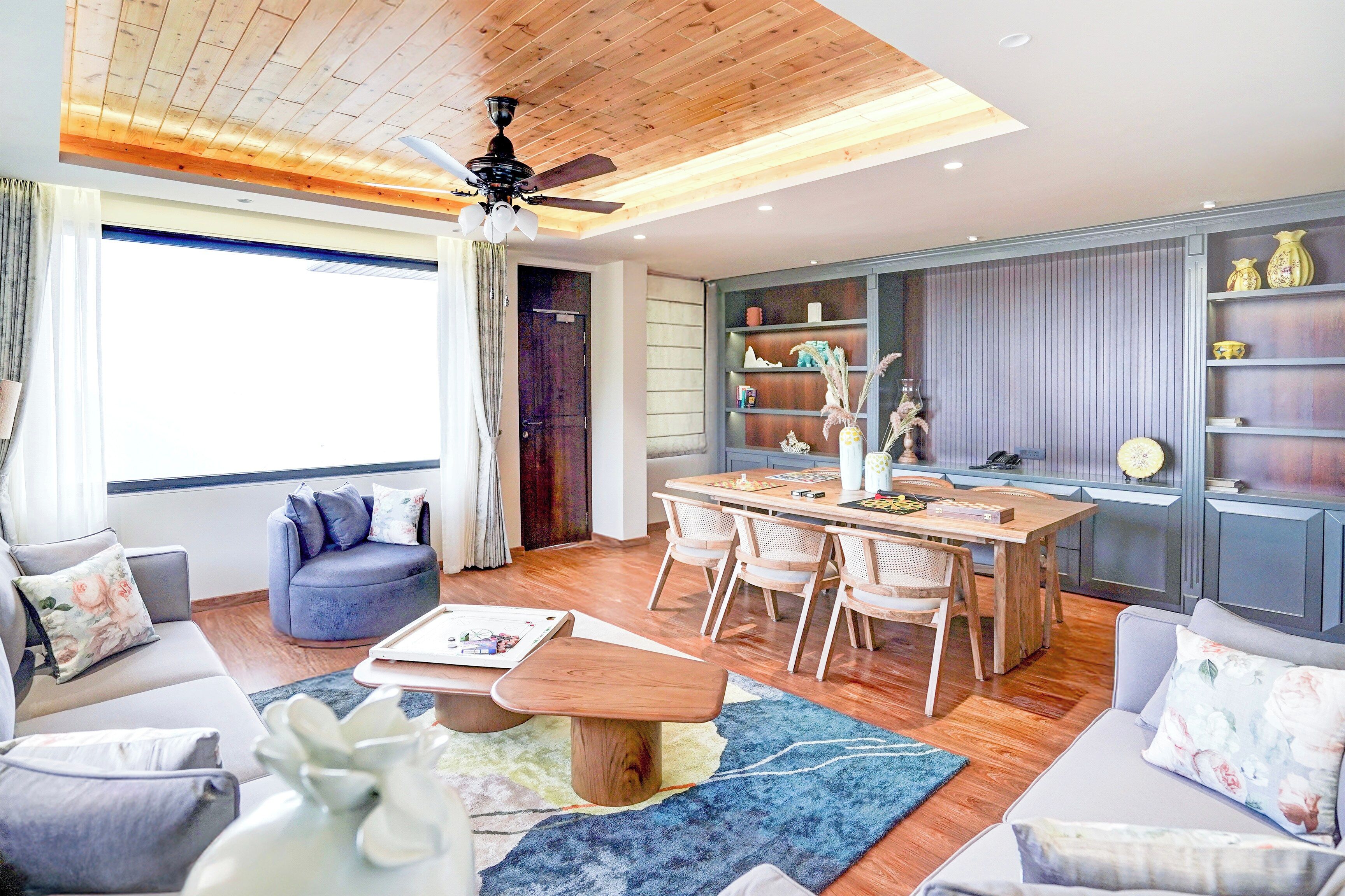 Una sala moderna con comedor, techo de madera y estanterías empotradas con objetos decorativos.