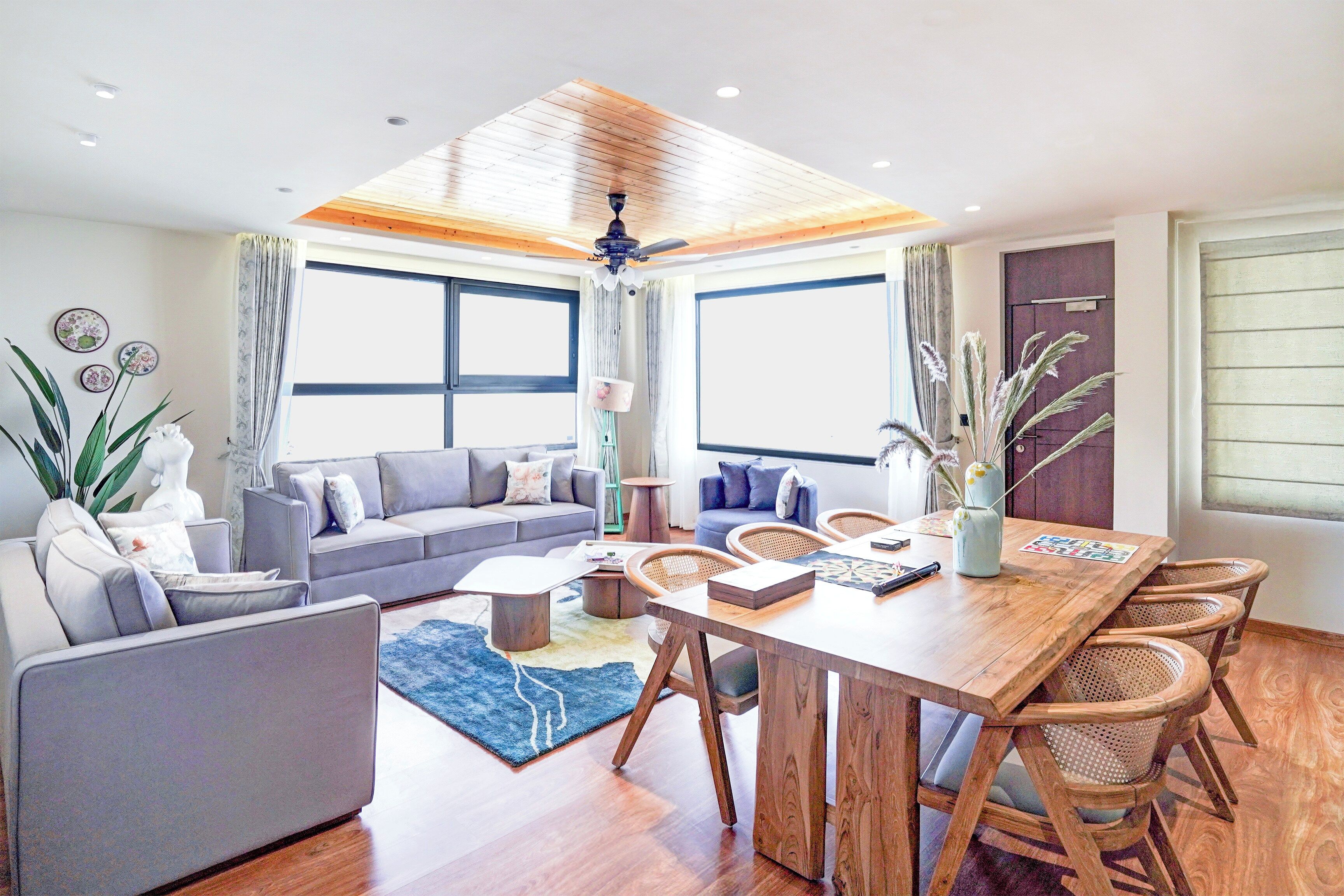 A modern living room with a grey sofa, wooden dining table, and wicker chairs.