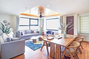 Uma sala de estar moderna com sofá cinza, mesa de jantar de madeira e cadeiras de vime.